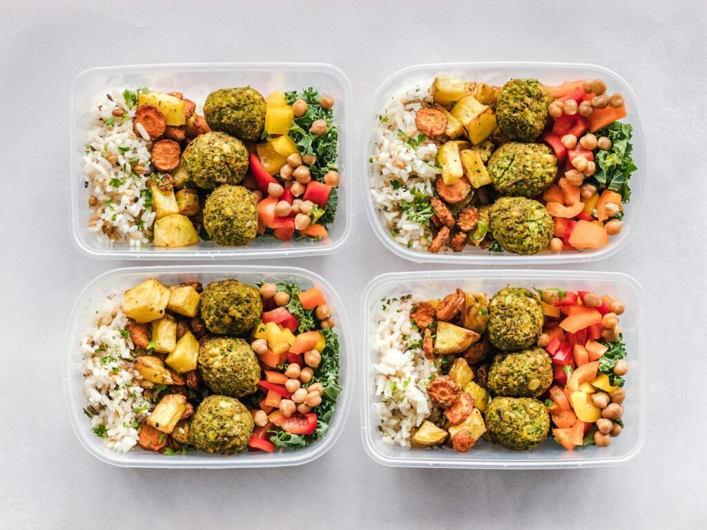 How To Stay Energized on Night Shifts: A Science-Backed Guide 5 Colorful meal prep containers with falafel, chickpeas, rice, and vegetables for a healthy lifestyle.