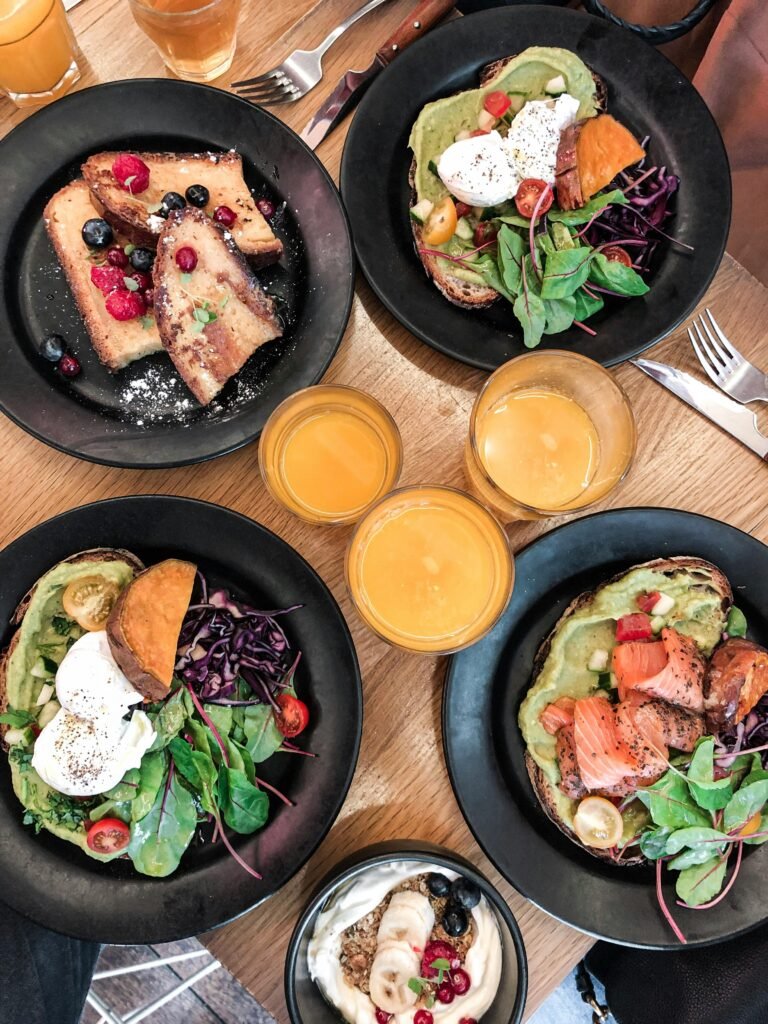 Home 2 Top-down view of a vibrant brunch spread featuring avocado toast, salmon, fresh salad, and juice.