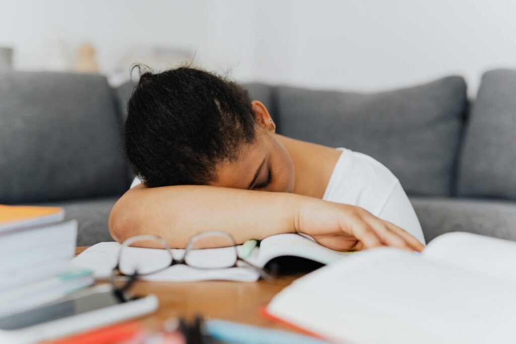 How To Stay Energized on Night Shifts: A Science-Backed Guide 7 A student falls asleep while studying at home, leaning on an open book with glasses visible.