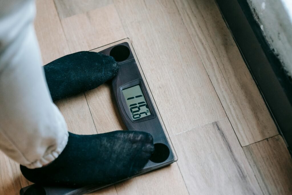 Stop Night Shift Weight Gain: 8 Proven Metabolism Boosters 1 From above of unrecognizable person in socks standing on electronic weighing scales while checking weight on parquet during weight loss