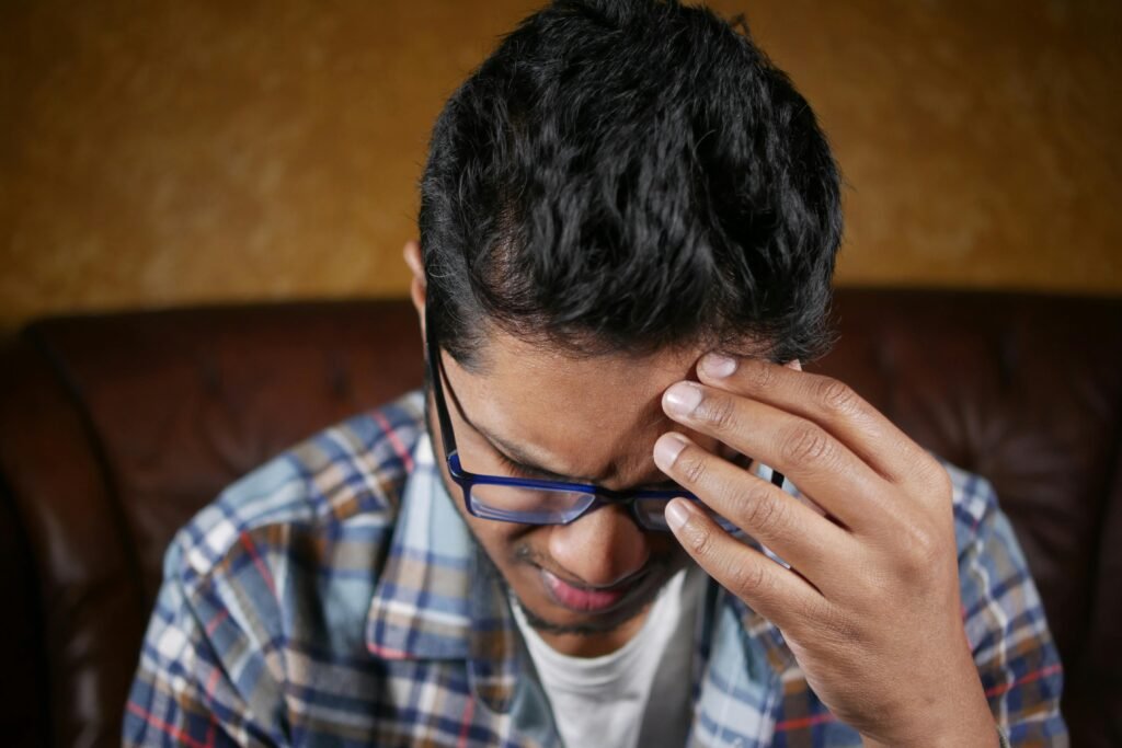 What to Do About Night Shift Memory Problems and Cognitive Decline 3 Close-up of a man wearing glasses, holding his head in pain, possibly experiencing a headache.
