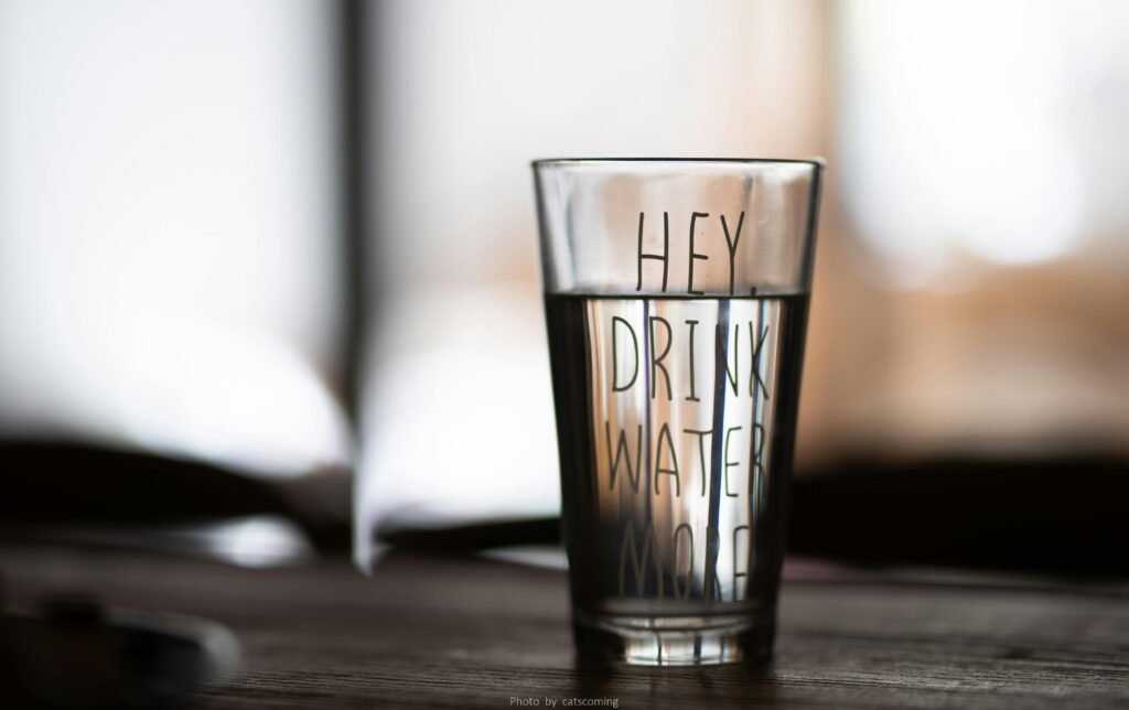 How to Manage Night Shift Digestive Problems 6 Close-up of a water glass with motivational text 'Hey Drink Water More' in a blurred indoor setting.