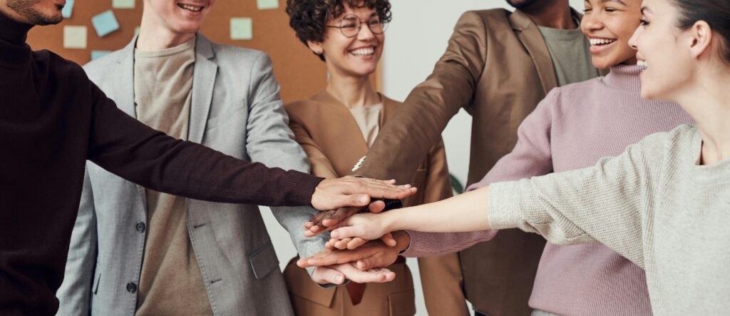 How to Stay Social and Connected in a Night Shift Lifestyle 2 A group of happy, diverse colleagues celebrating teamwork and cooperation with a group high five indoors.
