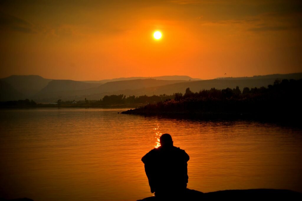How to Manage Night Shift Digestive Problems 7 A person sits alone by a tranquil lake, with a stunning sunset in the background.