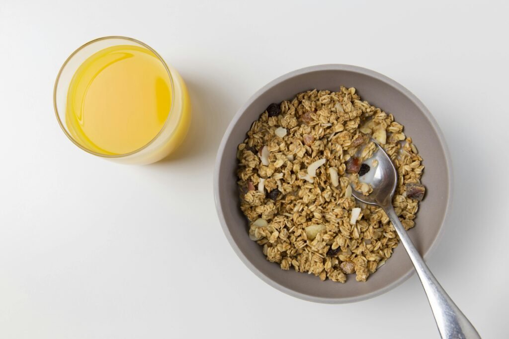 12-Hour Night Shift Meal Plan: Strategies to Stay Energized and Eat Healthy 6 A top view of granola in a bowl with a spoon and a glass of orange juice on a white background.