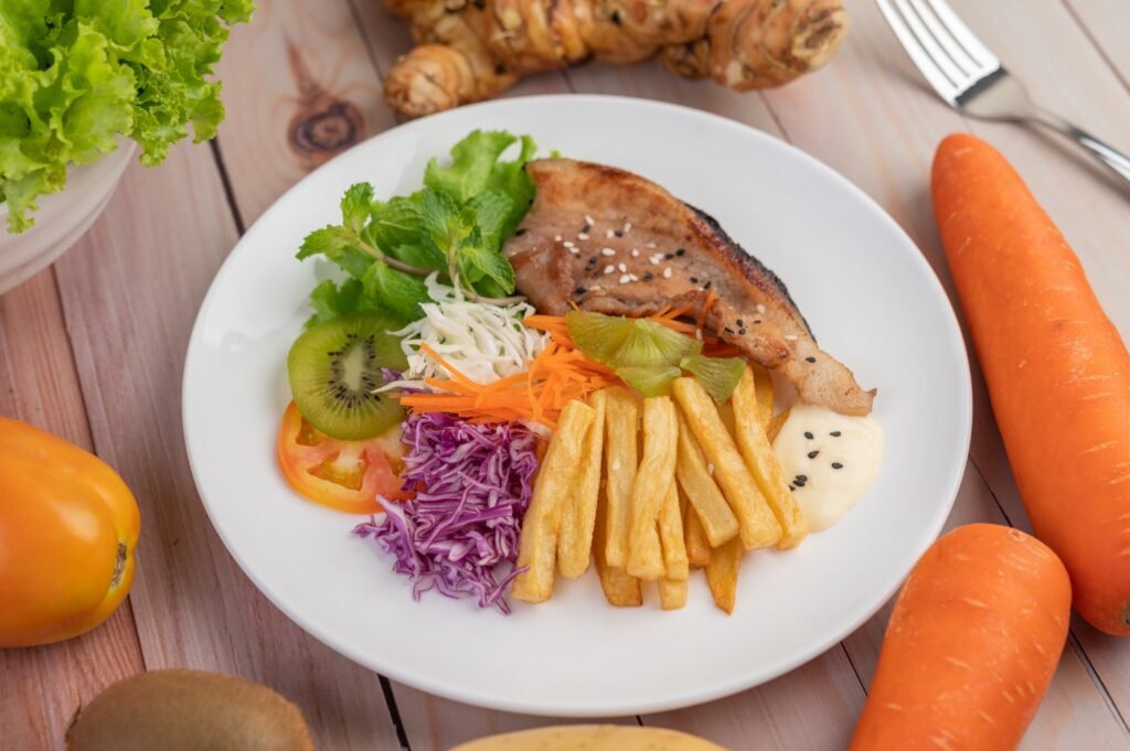 fish steak with french fries kiwi lettuce carrots tomatoes cabbage white dish 1